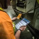 一名身穿橙色t恤的欧米茄澳门威斯人平台首页(ω澳门威斯人平台首页)员工正在对比设备标签和仓库里iPad上的信息